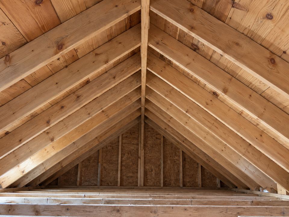 Paired timber rafters slope up to a ridge board beneath the roof decking inside an unfinished attic.