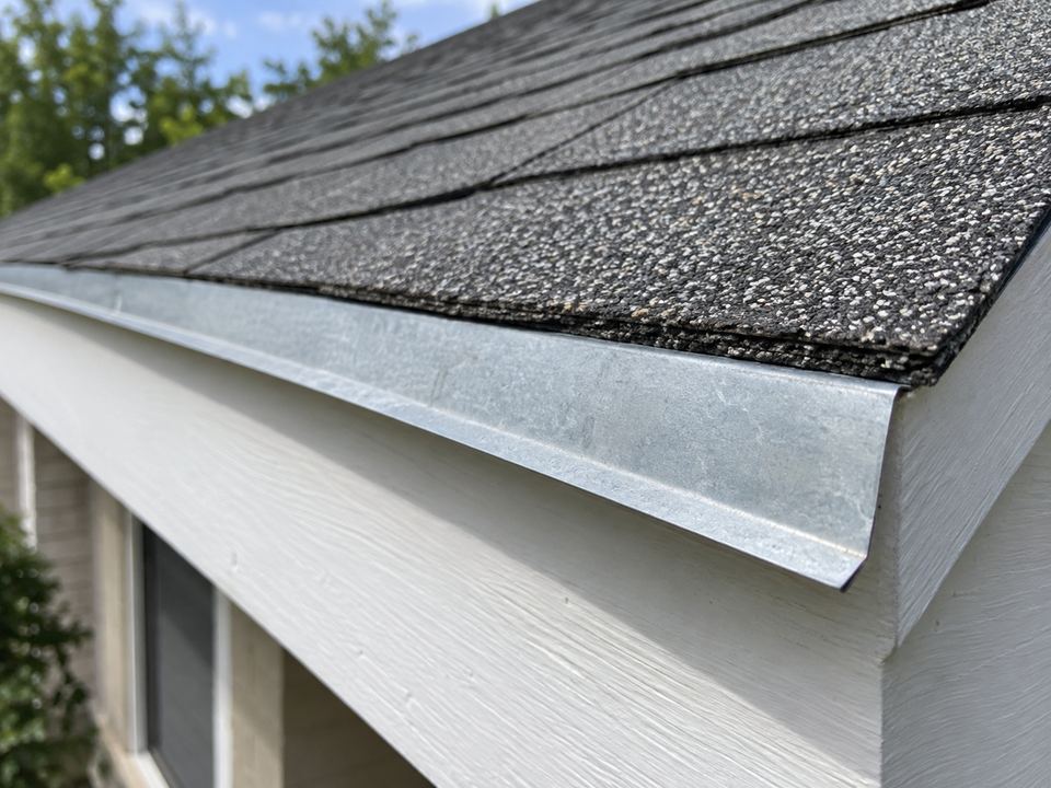 Bent metal drip edge beneath asphalt shingle ends, its lower lip projecting away from the white fascia board.