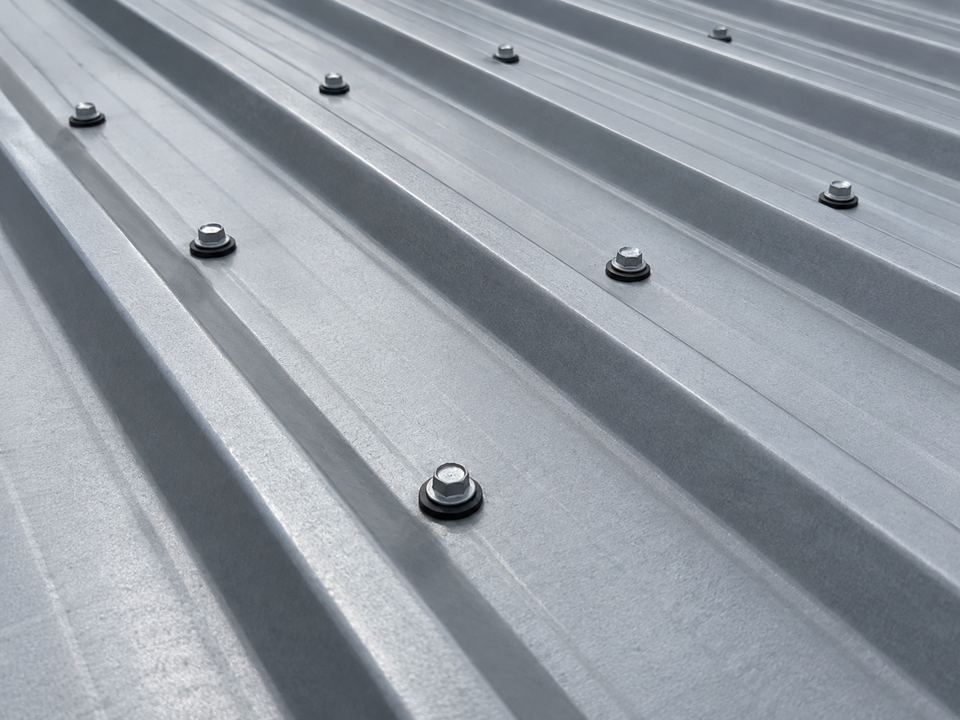 Hex-head screws with dark sealing washers are visible in the flat portions between raised ribs of metal roofing panels.