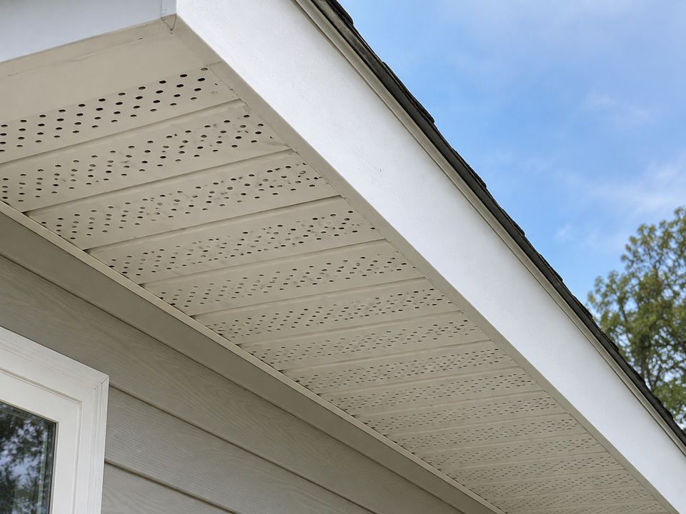 Perforated white soffit panels beneath an overhang meet a solid white fascia board along the outer roof edge.