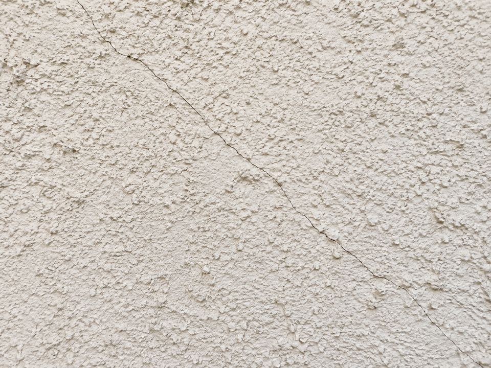 A narrow diagonal crack crosses a light-colored textured stucco surface.