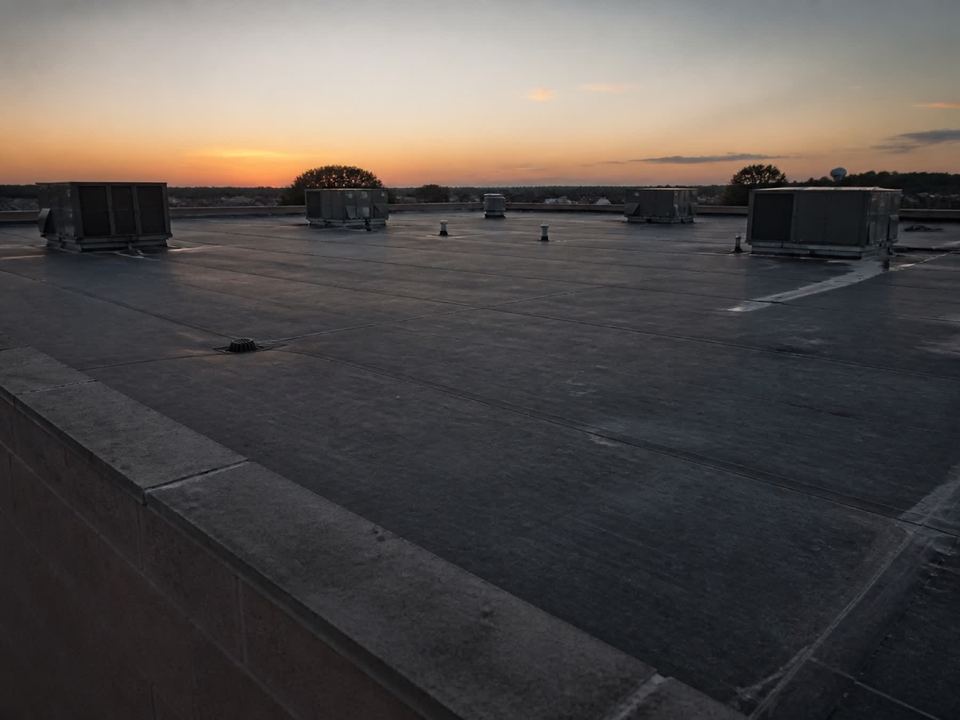 A low-slope commercial roof at dusk, mechanical curbs silhouetted against a warm horizon.
