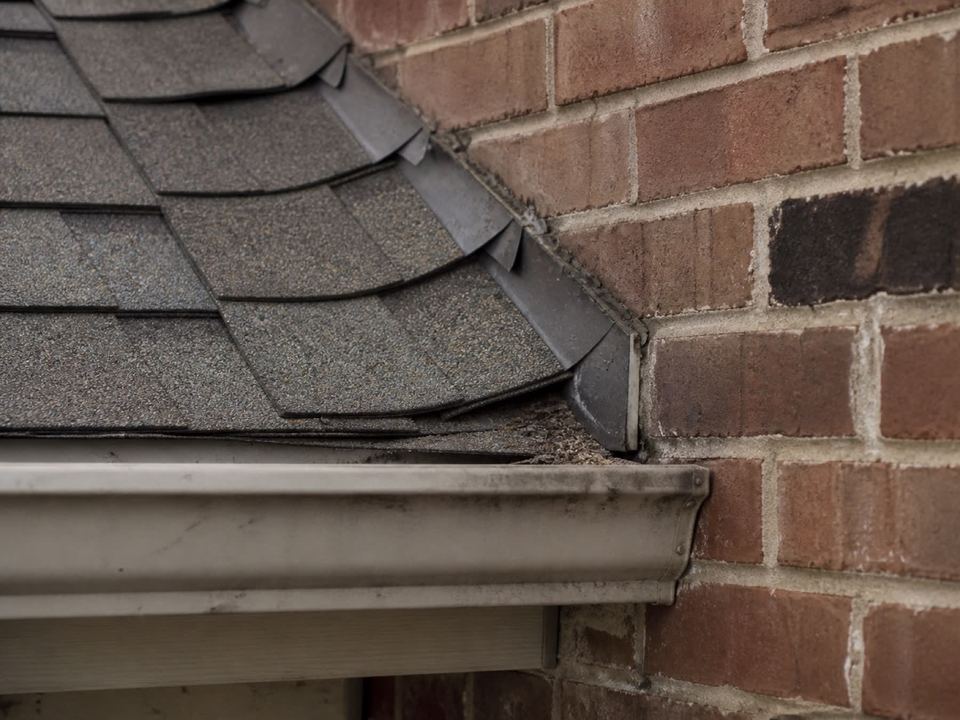 The junction where a roof edge, fascia, gutter and brick wall meet, step flashing visible under the courses.