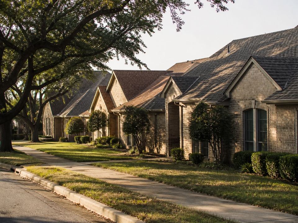 A North Texas residential street of brick homes with varied roof pitches in warm evening light.
