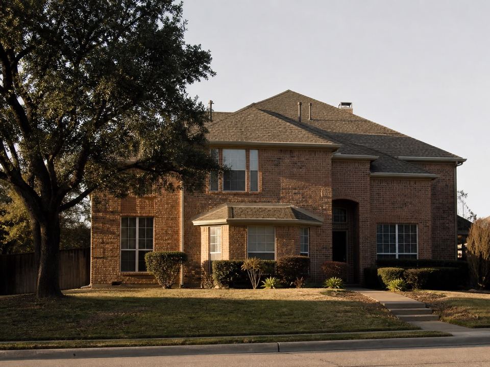 A two-storey brick North Texas home in late afternoon, the full roof visible with its hips, valleys and vents.