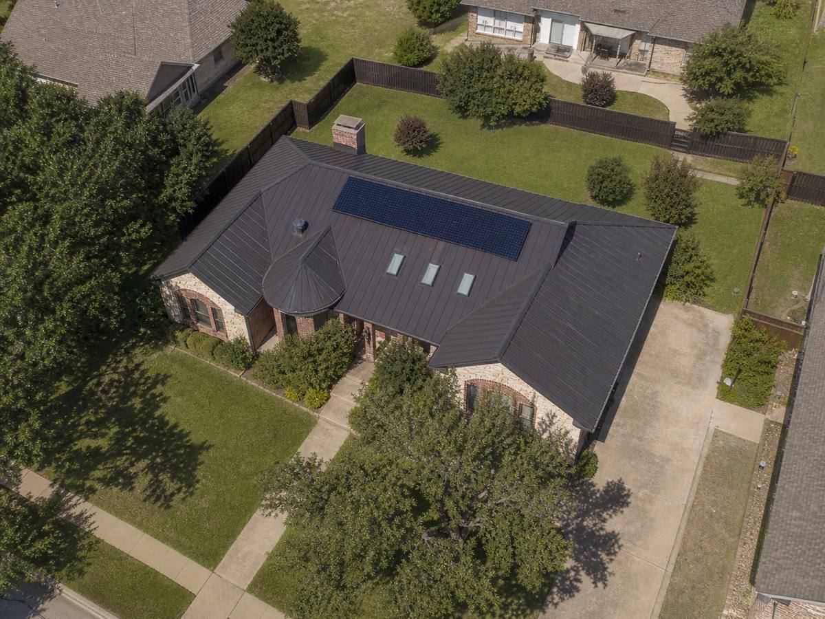 Overhead view looking straight down on a limestone-and-brick single-storey home with shallow cross-gables, showing the full run of matte bronze standing-seam metal and how the planes drain.