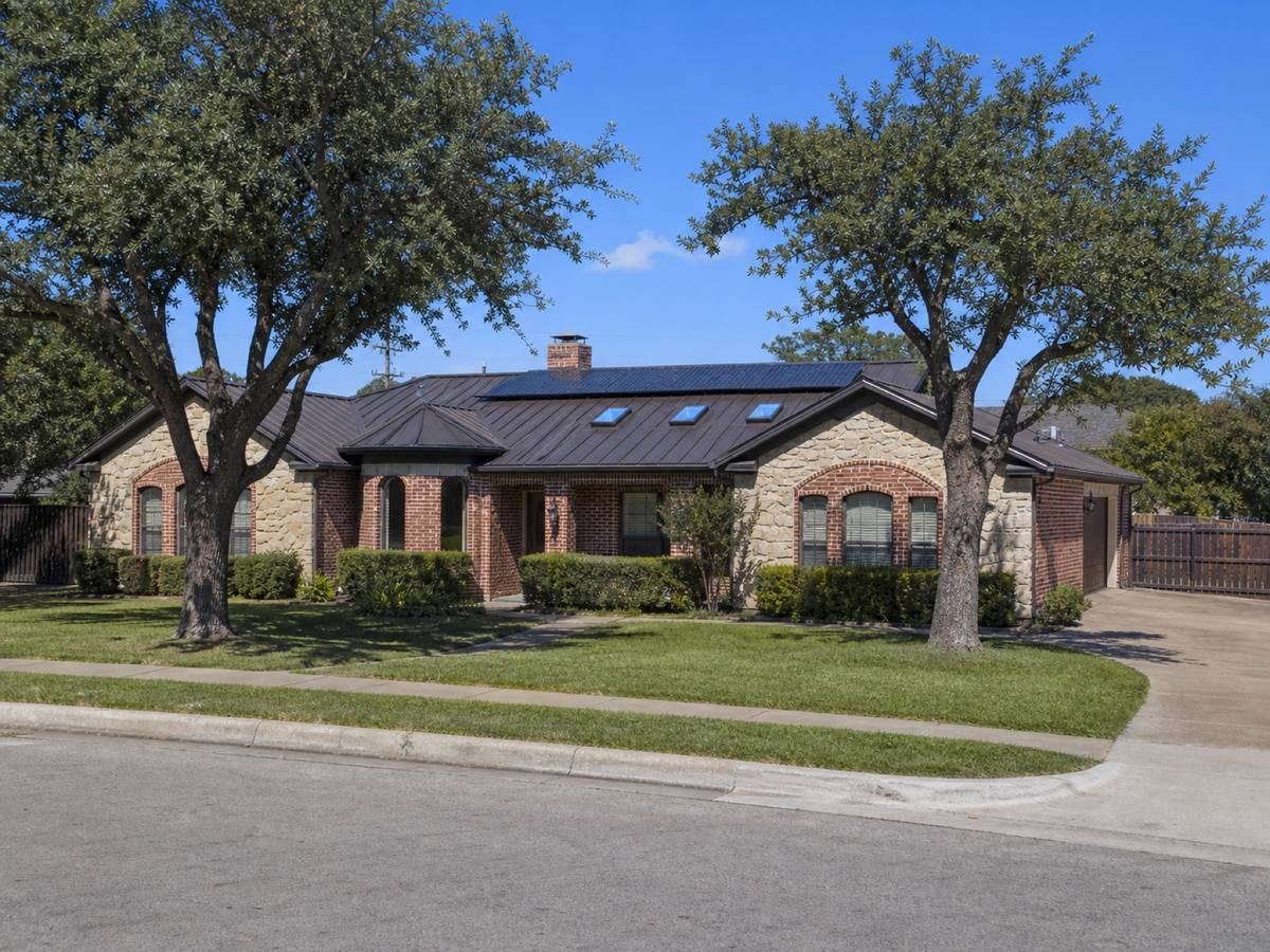 A limestone-and-brick single-storey home with shallow cross-gables seen from the street, the matte bronze standing-seam metal visible above the elevation.