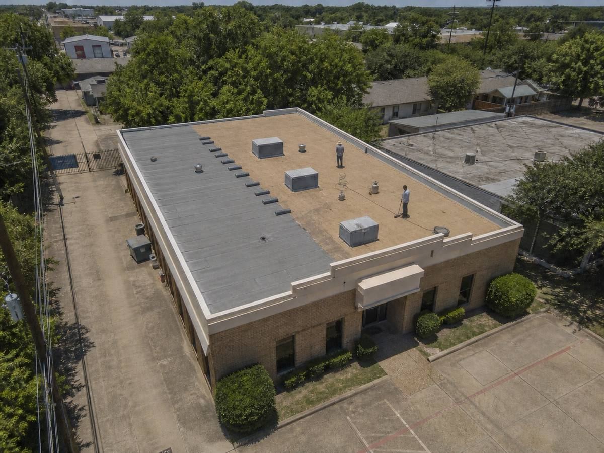 A small two-storey urban commercial building with a cream parapet part-way through a torch-down membrane installation, with finished and unfinished areas both visible.