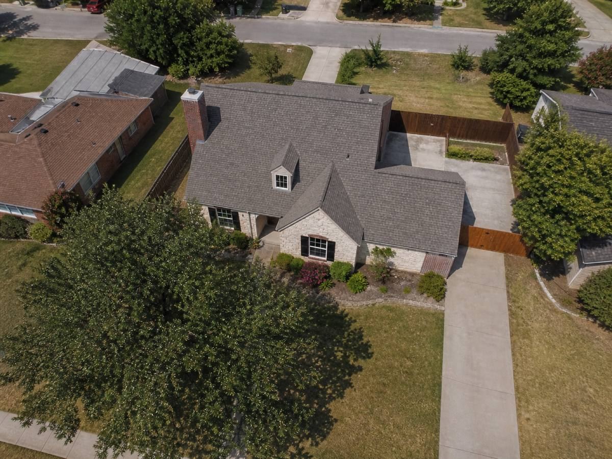Overhead view looking straight down on a one-and-a-half-storey house with a stone frontage and an offset garage, showing the full run of warm-grey impact-resistant shingles and how the planes drain.
