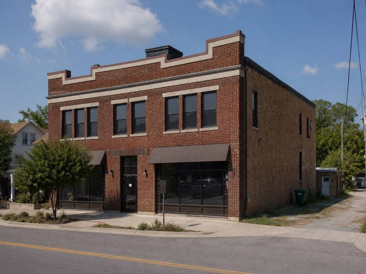 A mixed-use brick building with a stepped parapet seen from the street, the a dark-grey low-slope membrane visible above the elevation.