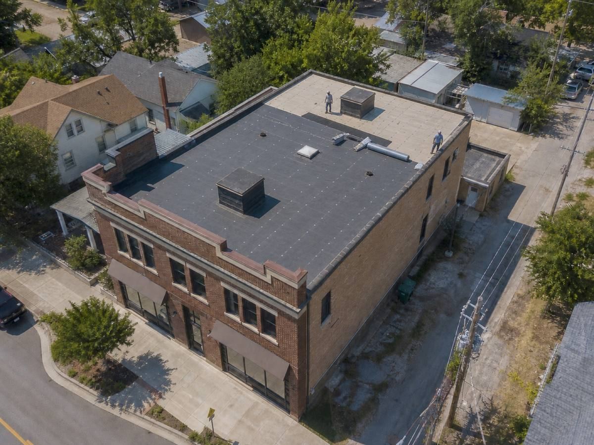 A mixed-use brick building with a stepped parapet part-way through a modified bitumen installation, with finished and unfinished areas both visible.