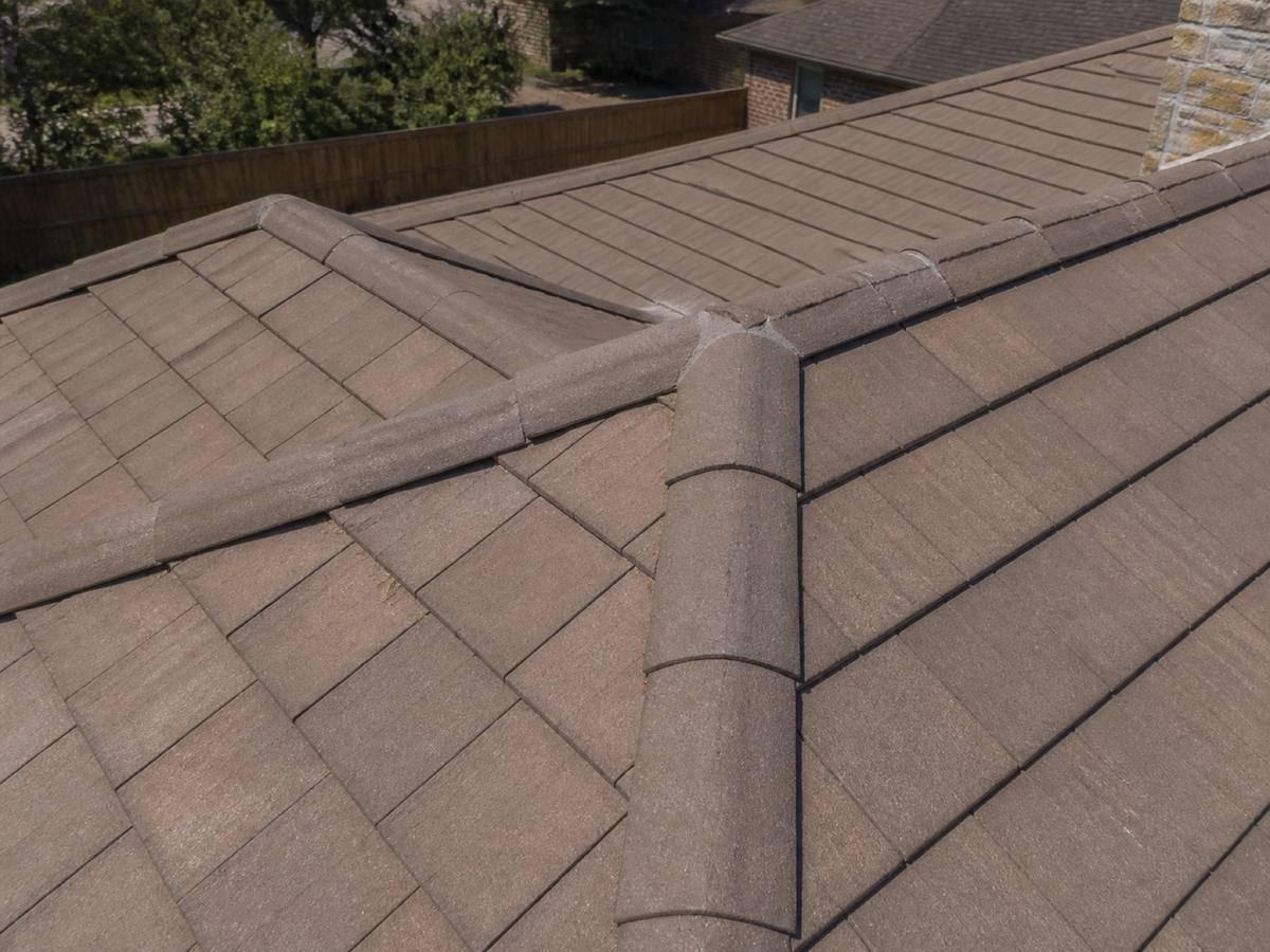 Flat concrete roof tiles with barrel-profile hip and ridge caps meeting at a junction, mortar visible where they join.