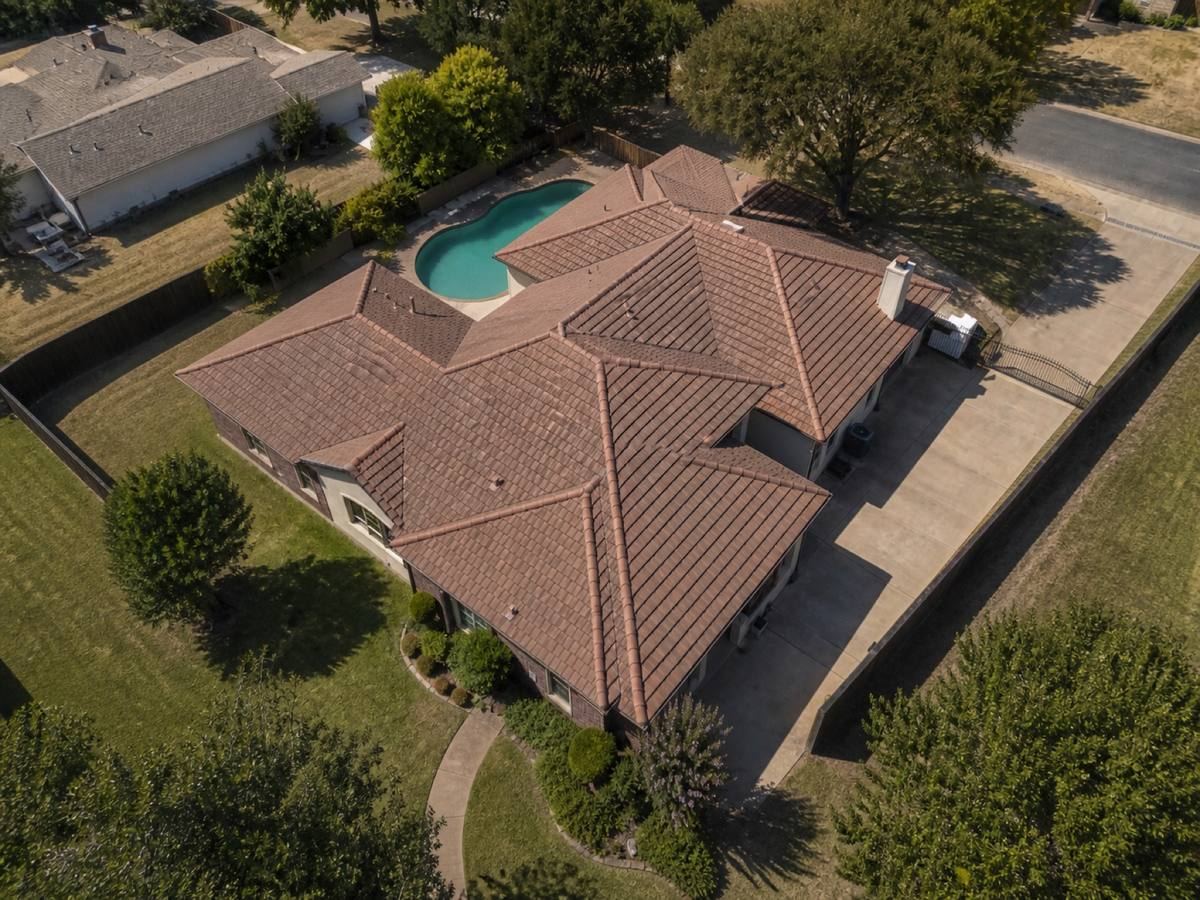 Overhead view looking straight down on a cream stucco-and-brick house with low hips and a rear pool, showing the full run of weathered terracotta concrete tile and how the planes drain.