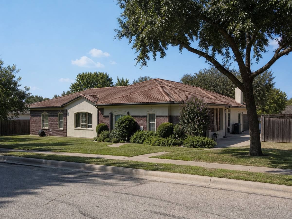 A cream stucco-and-brick house with low hips and a rear pool seen from the street, the weathered terracotta concrete tile visible above the elevation.