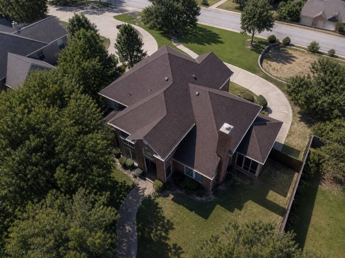 Overhead view looking straight down on a large brick house with multiple hips and a screened rear porch, showing the full run of deep-brown architectural shingles and how the planes drain.