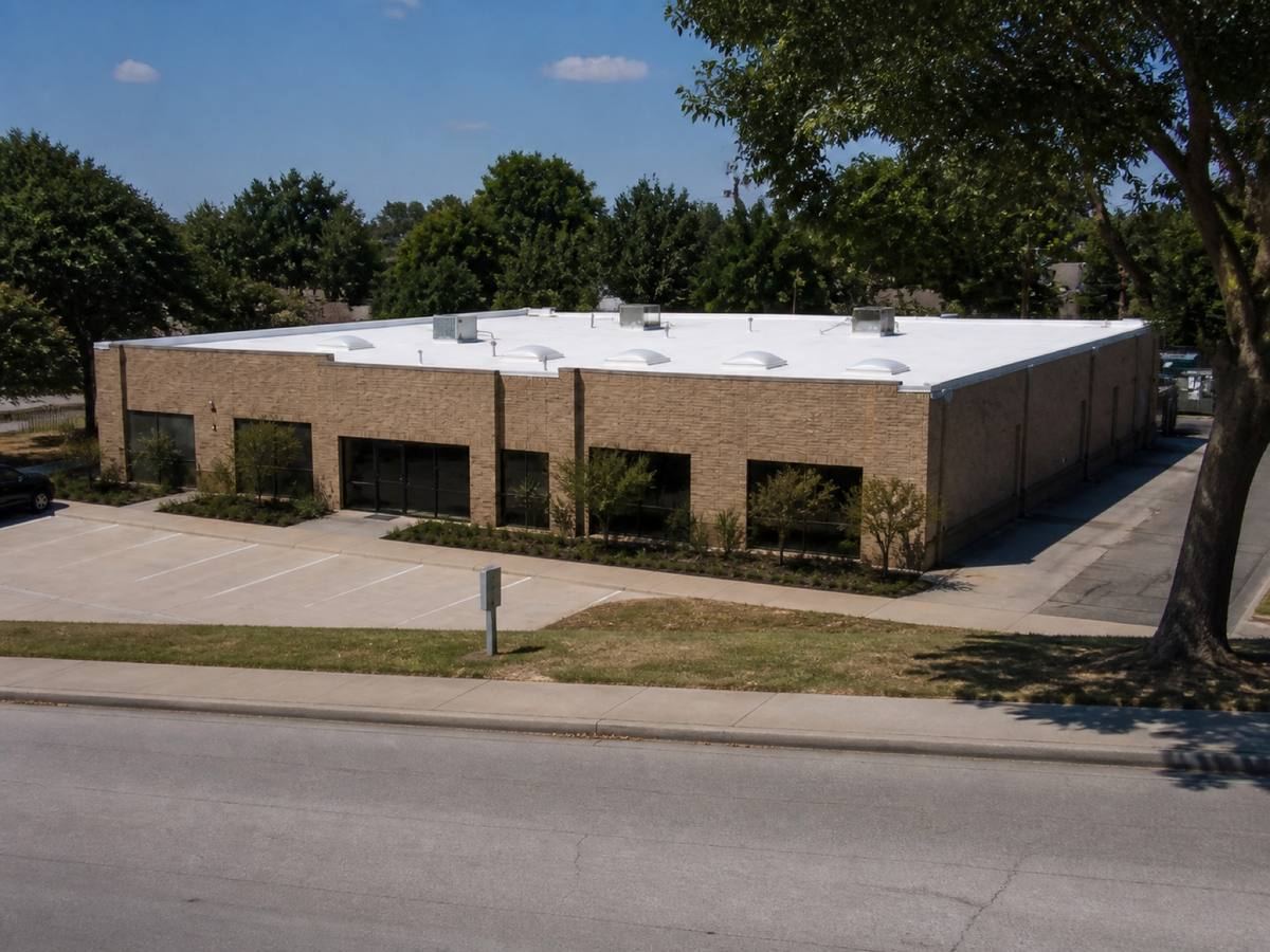 A single-storey brick retail building with a rectangular roof seen from the street, the a white TPO membrane visible above the elevation.