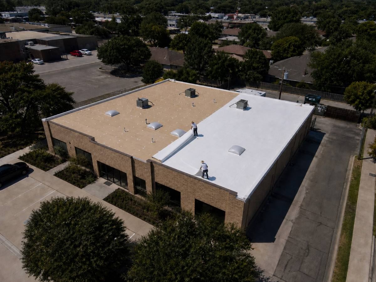 A single-storey brick retail building with a rectangular roof part-way through a tpo membrane installation, with finished and unfinished areas both visible.
