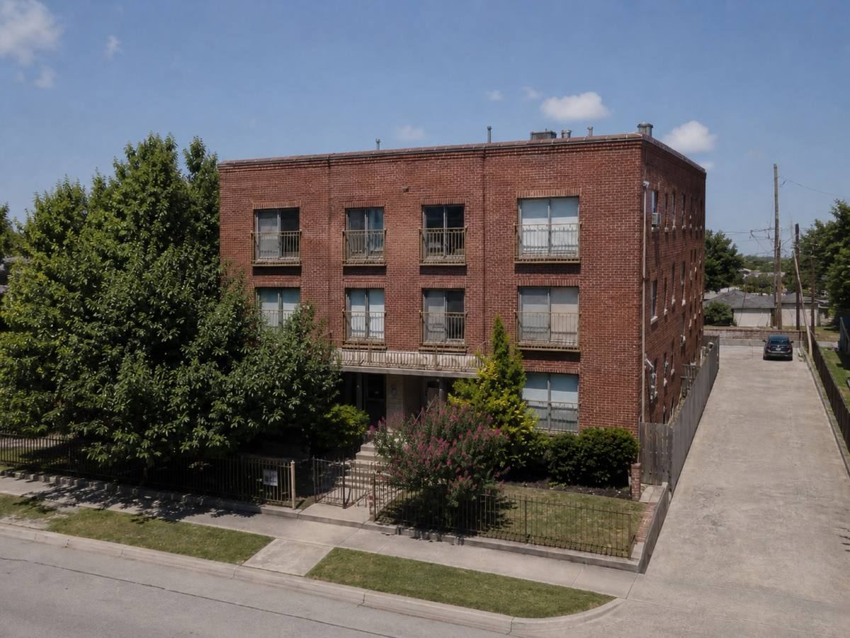 A compact brick apartment building with parapets on all sides seen from the street, the a medium-grey modified-bitumen cap sheet visible above the elevation.