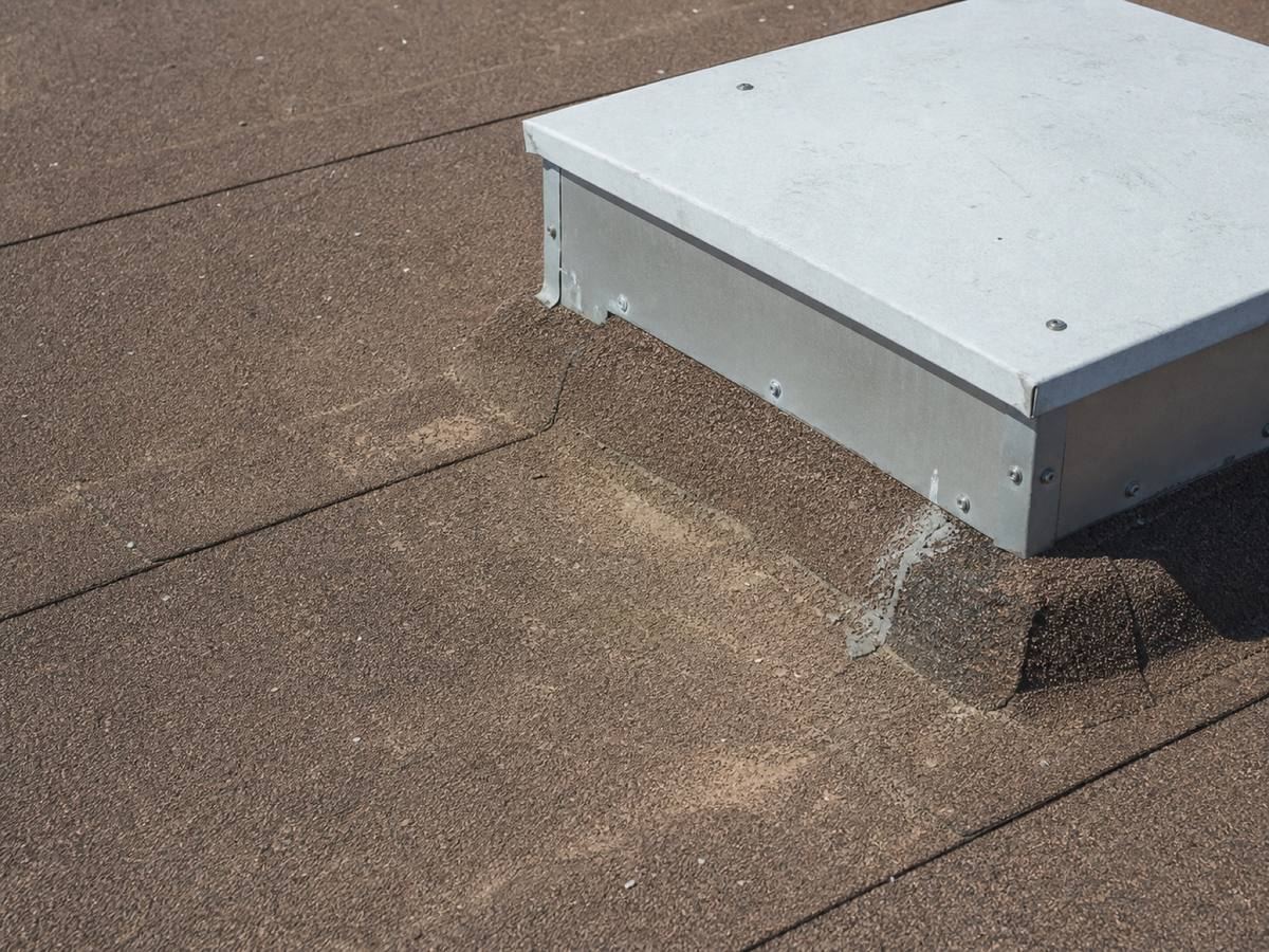 A metal equipment curb on a granulated cap-sheet membrane roof, the membrane flashing dressed up the base of the curb.