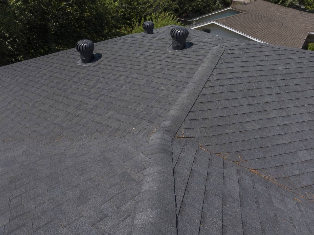 Close view of a shingle field running to a ridge, the courses even and the ridge cap seated over them.
