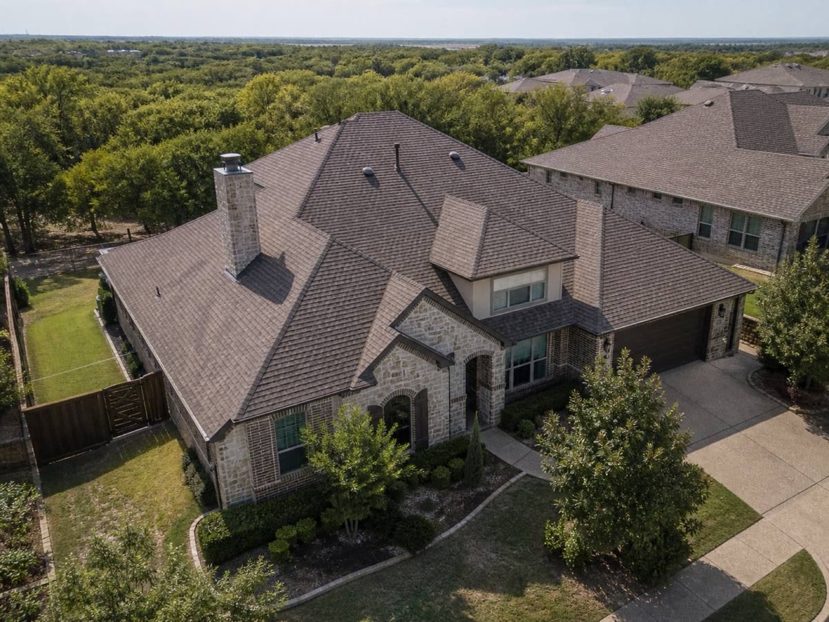An oblique aerial view of a two-storey stone-and-brick house with a complex roof of many hips, valleys, dormers and a chimney.