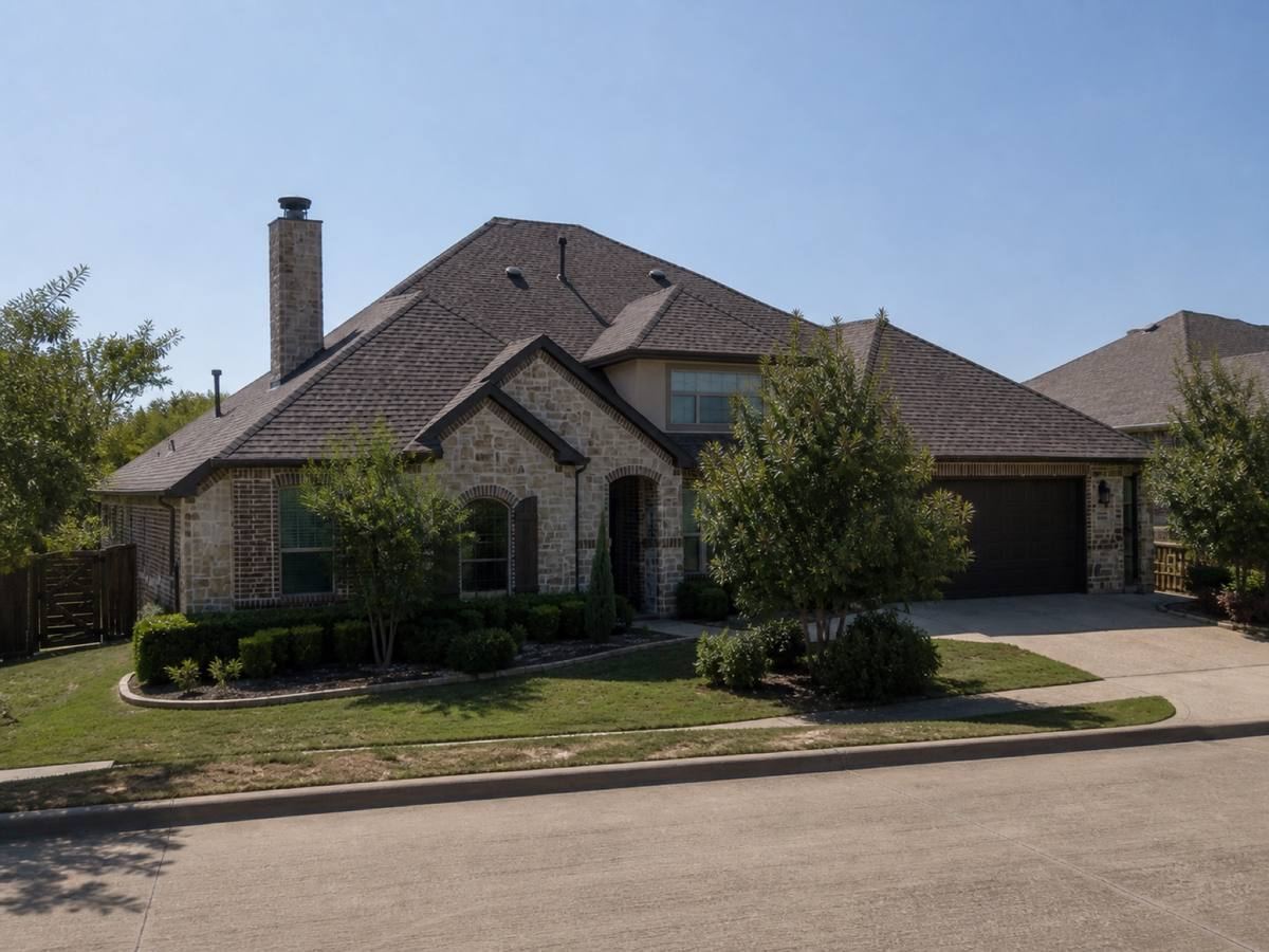 A stone-and-brick house with a broad hip roof backing onto a greenbelt seen from the street, the weathered-brown dimensional shingles visible above the elevation.