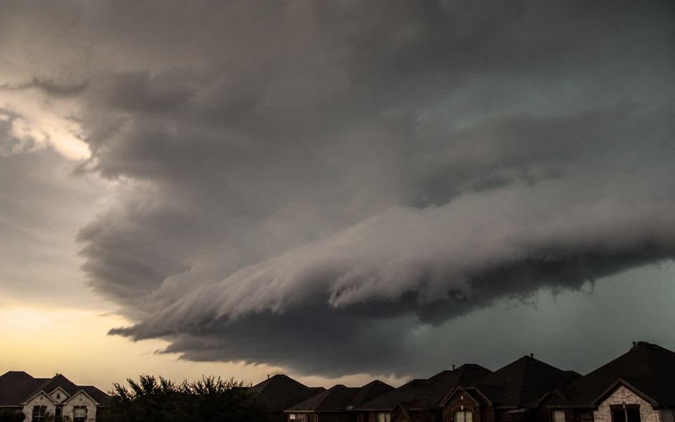 A storm cell building over a row of low suburban rooflines.