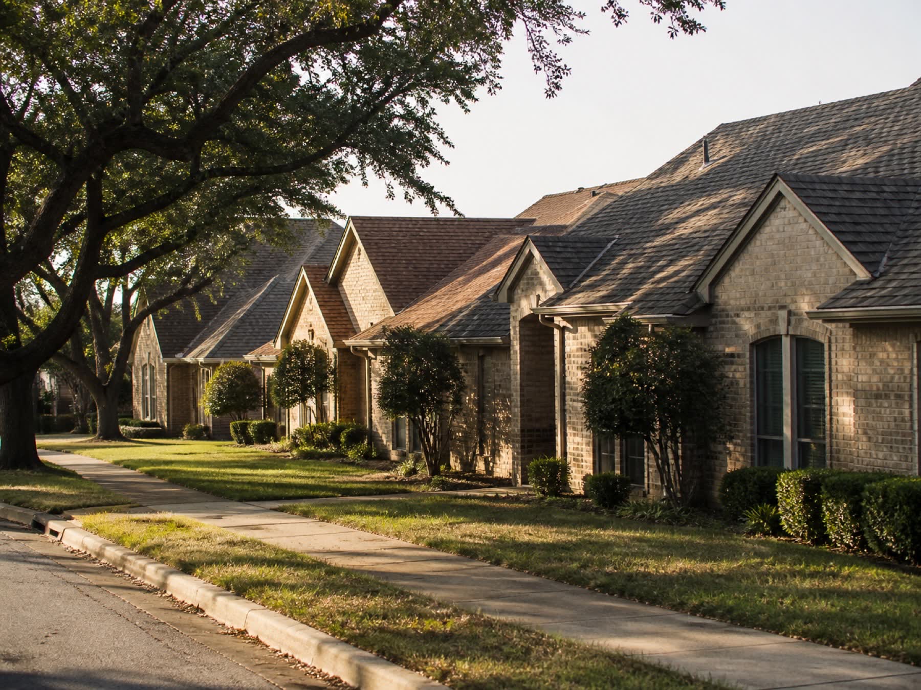 A North Texas residential street of brick homes with varied roof pitches in warm evening light.